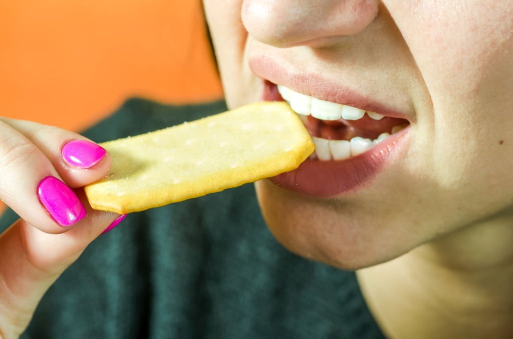 Close up of a young girl lips and teeth eating cookie or biscuit, selective focus